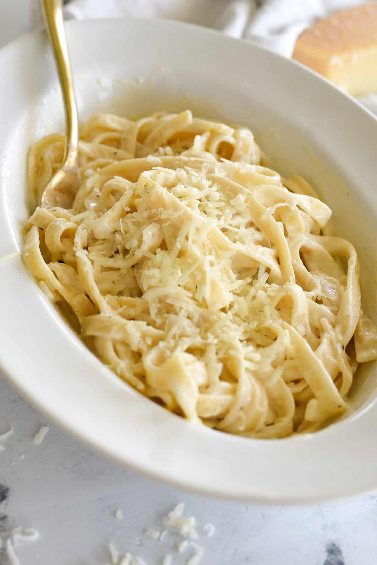 bowl of alfredo sauce over fettucine with parmesan cheese on top