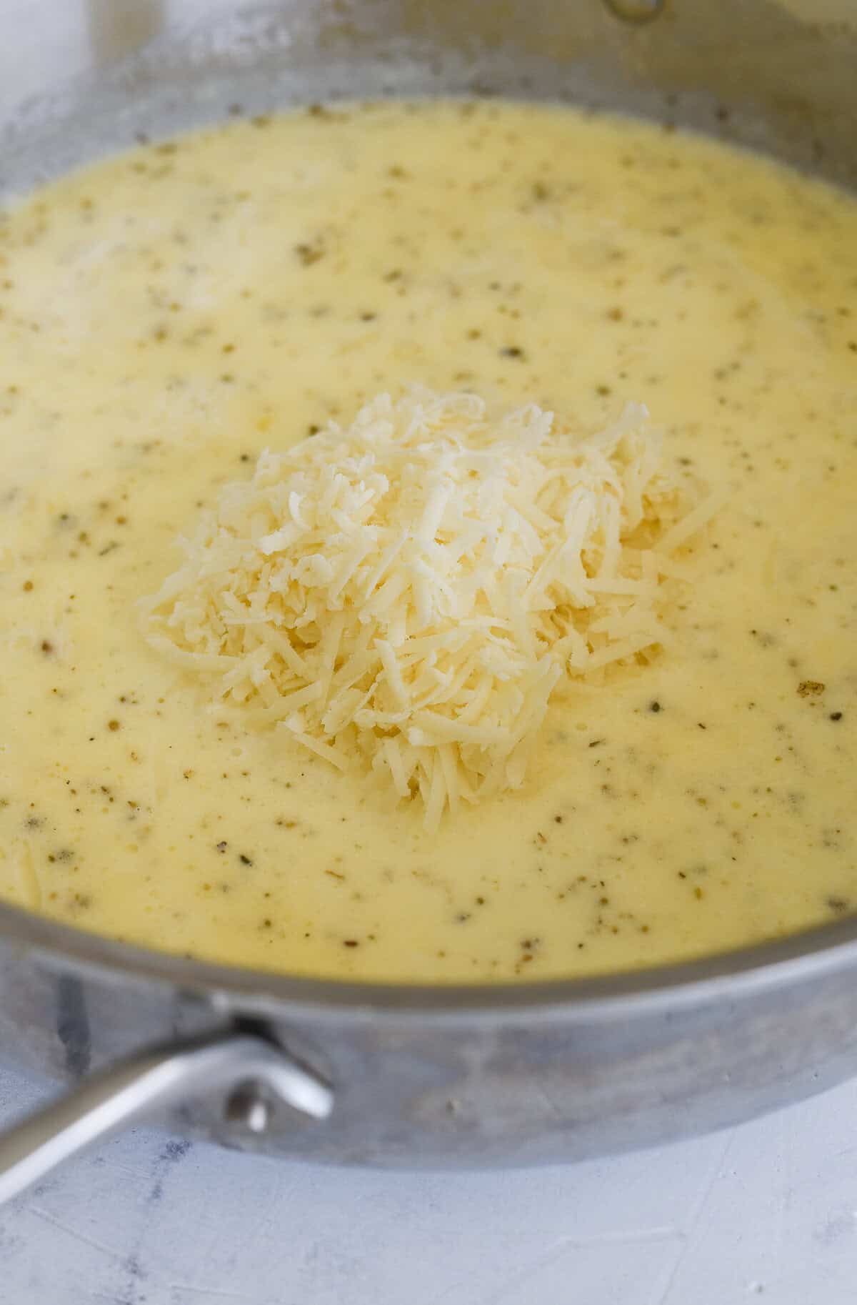 adding cheese to alfredo sauce