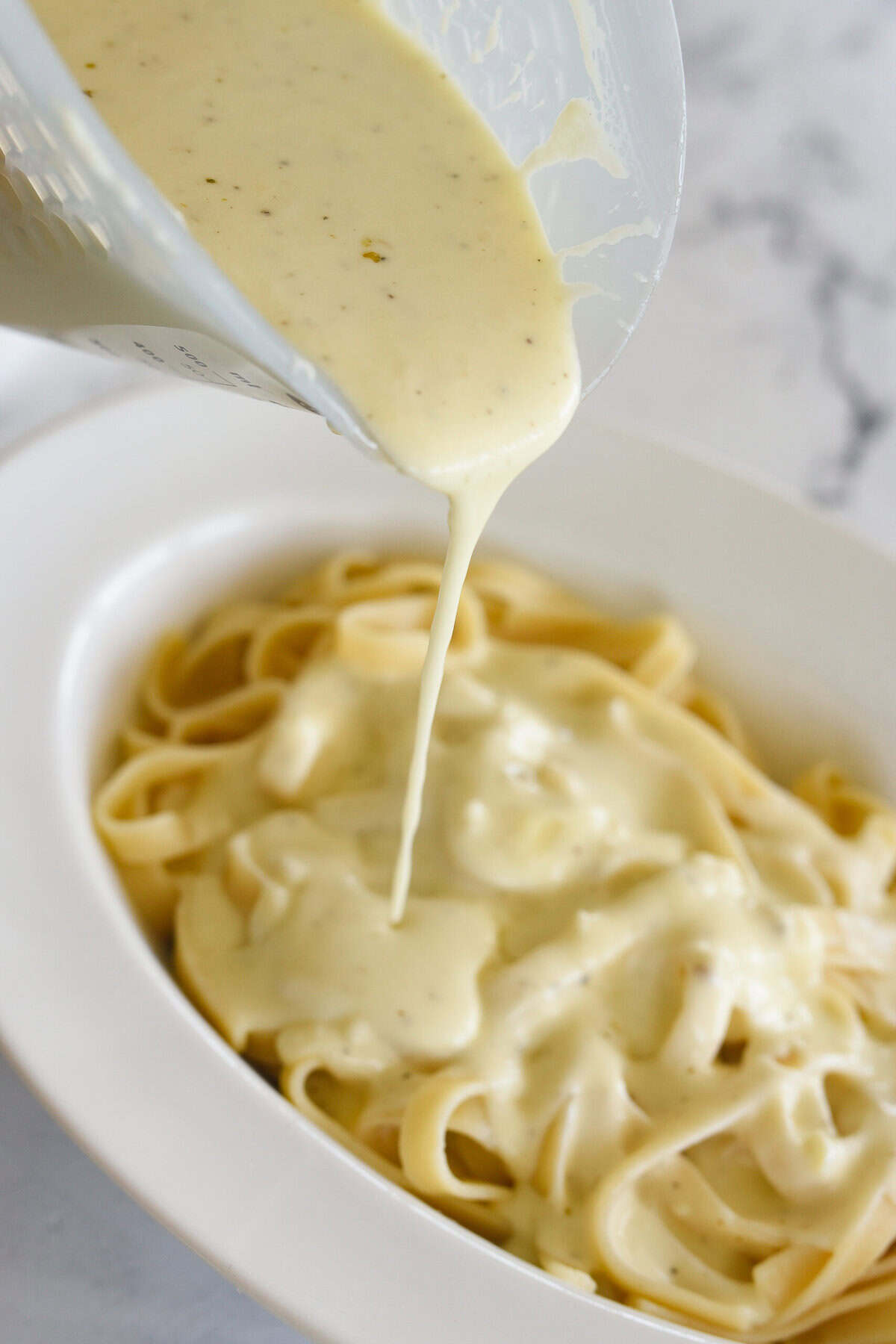 pouring alfredo sauce over pasta