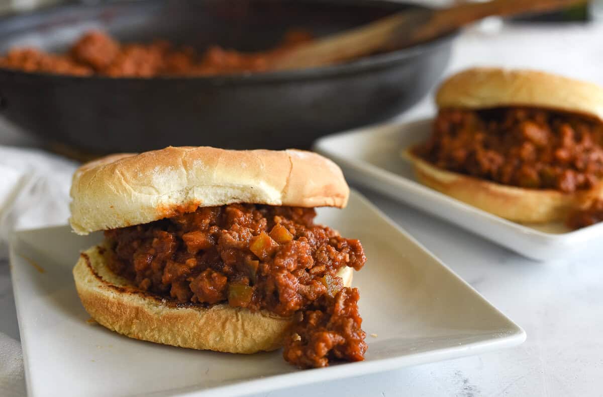 two sloppy joe sandwiches on buns on white plates