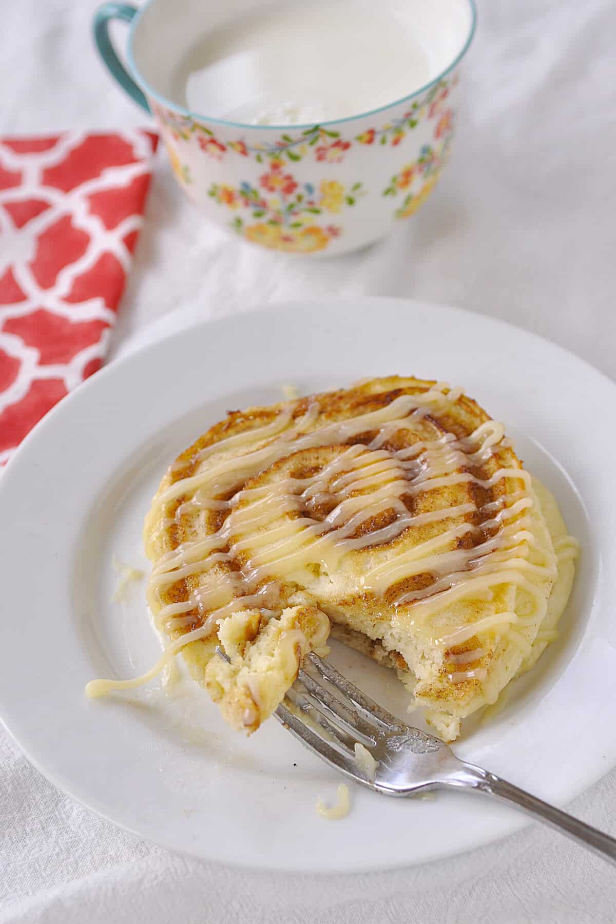CINNAMON Roll pancakes with a bite out of it on a plate with a fork